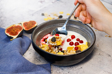 the hand of an invisible person with a spoon next to a plate in which there is a granola with yogurt and berries.next to figs and a napkin. High quality photo