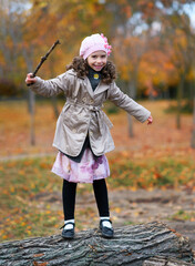 Fototapeta premium Portrait of a girl in an autumn park. The child is standing on the trunk of a tree and playing with a twig
