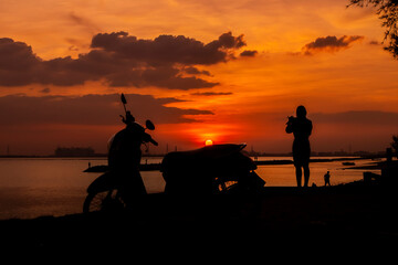 Fototapeta na wymiar A woman driving a motorbike waiting for someone by the sea at sunset.