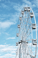 Ferris wheel over background of beautiful blue sky with fluffy clouds.