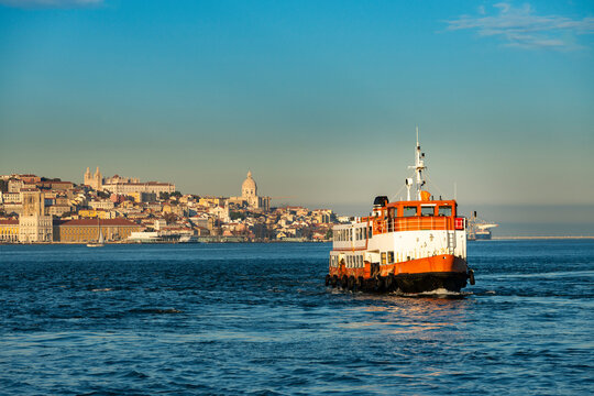 A traditional cacilheiro ferry boat crossing the Tagus River (Rio Tejo) with the city of Lisbon skyline on the background, in Portugal
