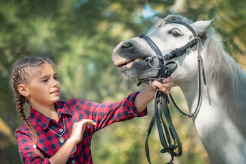 a teenage girl is afraid of a horse while training and caring for a pony. She holds the animal by...