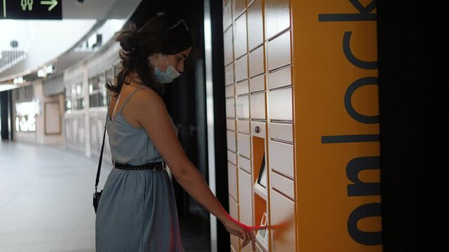 mail delivery and post service concept - happy woman in medical mask taking boxes from automated parcel machine terminal in shopping mall, coronavirus pandemic, life after covid 19.
