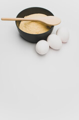 dark stoneware bowl with flour wooden spoon and white eggs on a white tabletop