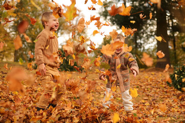 Outdoor fun in autumn. Children playing with autumn fallen leaves in park. Happy little friends.