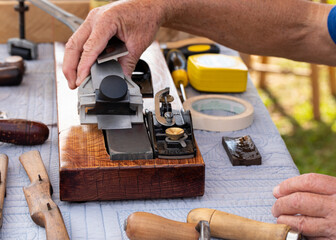 Senior man sharpens a wood plane blade on a mounted whetstone.