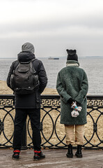 A man and a woman walking along the river embankment on a gloomy day