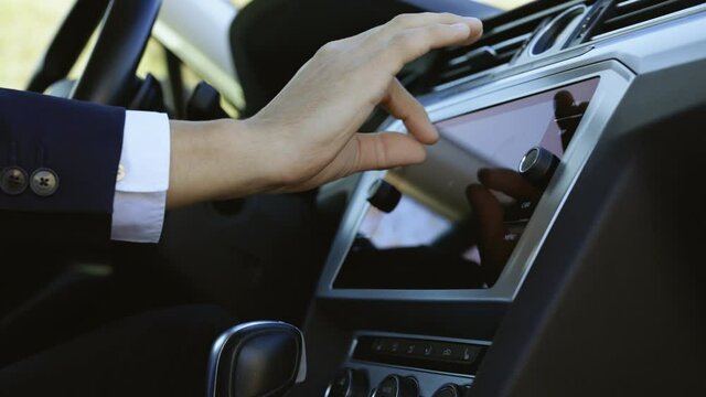 Male man hand touching, tapping, zoom out on screen monitor on modern luxury car. Interface concept. Unknown young man sitting in front of the handlebar of his own luxury auto and applying navigator