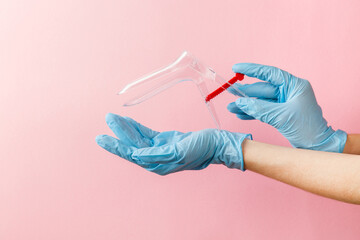 Gynecological speculum in woman's hands in medical sterile gloves. Female health concept. Preventive gynecological examination. Prevention for womens health. Vaginal examination on pink background