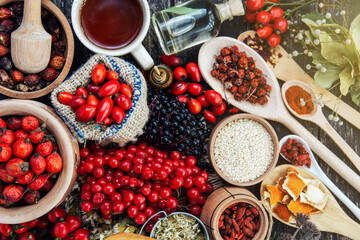 herbal tea cup Dog rose, bunch branch Rosehips, types Rosa canina hips, dry orange peel, tea leaves essential oil and hot on dark background. Medicinal plants and herbs composition