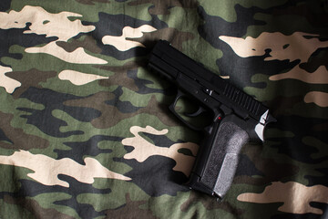Black handgun on military camouflage green, brown, beige and black fabric