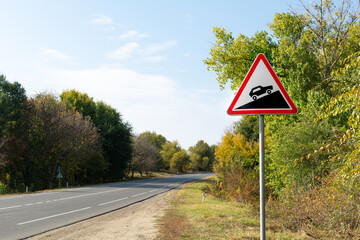Triangular road sign steep climb against the background of autumn trees near the track
