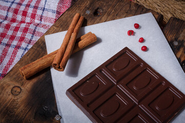 Bar of dark bitter chocolate with chilly pepper, cinnamon, red pea pepper flavour on white paper,...