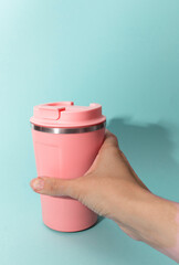Hand holding a thermo coffee mug on blue background