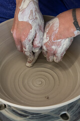 Pottery on a spinning wheel with a spiral being sculpted by hands. Movement can be seen as a spiral in the clay bowl is produced.