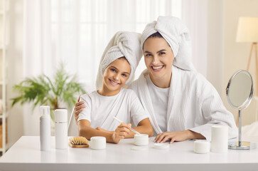 Our beauty moments. Portrait of young mother and her teenage daughter who have organized home beauty salon and spend spa day together. Mom and daughter in morning with drops of cream on their noses.