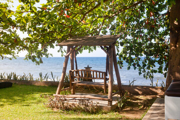 Old wooden bench swing under tree in the garden. Swing on the seashore.
