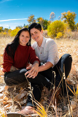 Lesbian couple holding each other in a field during autumn surrounded by leaves and smiling. 