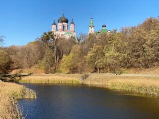 Obraz premium Beautiful Church on river bank. St. Panteleimon’s Convent Monastery Ukrainian Orthodox Church over Feofaniya park in Kyiv city, Ukraine. Idyllic sunny autumn day near pond in scenic park in Kiev town.