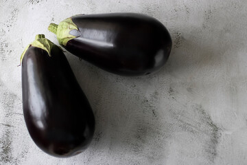 Two ripe eggplants on a gray cement background.