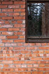 A fragment of the wall of an old brick house with a broken window. Metal grating on the window with broken glass