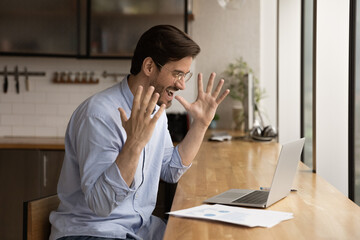 Happy young businessman entrepreneur worker in eyeglasses looking at laptop screen, celebrating...