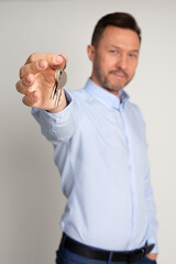 Photo of employee manager in shirt of real estate agency holds in hands keys to appartments. Buying or renting house. man is happy to become home owner. Studio shot on neutral background.