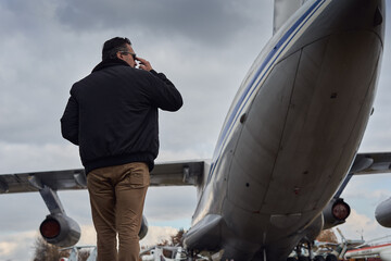 Oldschool pilot in the bomber jacket posing near the aircraft, aviator male with scarf and...