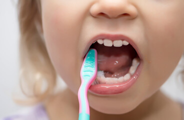 A little girl brushes her teeth with a toothbrush for children, close-up. Oral hygiene.