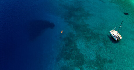 Fototapeta na wymiar Aerial photo of yellow canoe close to catamaran boat at tranquil paradise turquoise water in Ithaca Greece