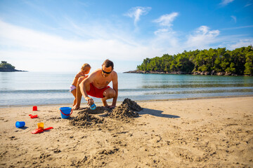 Father and daughter building sand castle on the beach at sunny day. 