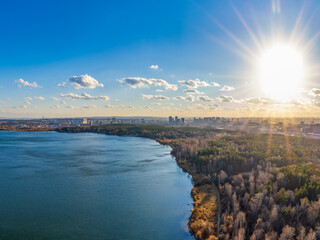 Autumn forest on lake shore at sunset and city on horizon, auerial view