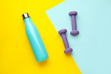 Dumbbells and bottle of water on color background