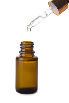 Dripping of essential oil from pipette into bottle on white background