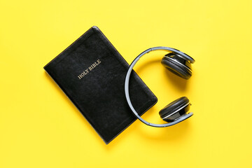 Holy Bible and modern headphones on color background