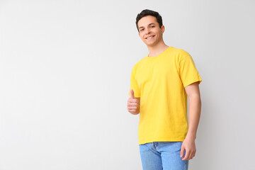 Handsome young man in stylish t-shirt showing thumb-up on light background