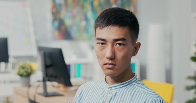 Close-up of the face of a man of Korean Japanese Asian beauty, he looks into the camera with dark eyes, sighs, sad, angry, disappointed, loss of employment, job, failure