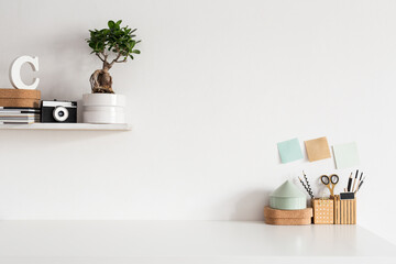 Stylish home office desk. Workspace with office supplies and accessories on a shelf and copy space or mockup against white wall background. Creative workplace.