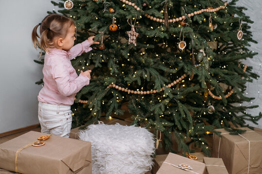 Cute Toddler Child Waiting For Presents At Home After Decorating Christmas Tree In Eco Style With Wooden Toys. Xmas Evening For Kids. Nordic Style Calm Preparation. Sad Girl