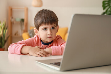 Little boy watching cartoons on laptop at table in living room