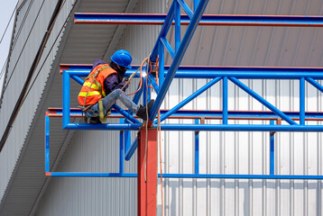 Low angle view of construction worker with safety equipment welding metal on roof structure of...