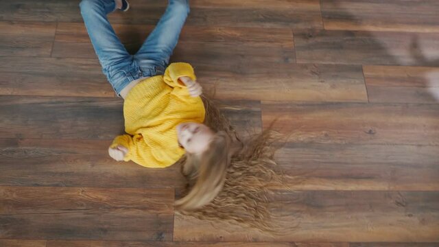 The Energetic Cheerful Teenage Girl is Having Fun, Fooling Around, Making Arbitrary Movements on the Floor of the House. Crazy Movements, Fun, Relaxation, Good Mood. Mental Health. View From Above.
