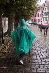 Portrait on back view of woman wearing a green rain coat poncho in the street - obrazy, fototapety, plakaty