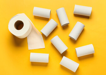 Roll of toilet paper and empty cardboard tubes on yellow background