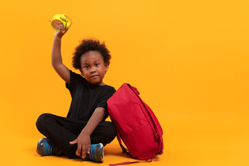 Black child boy 3 years, Student kid holding an alarm clock in his hand while sitting with red...