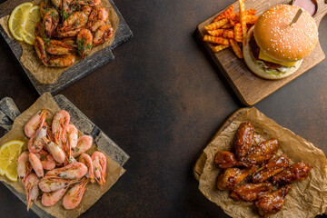 boiled shrimps with lemon, fried shrimps, burger and chicken wings bbq, on concrete brown table top view with copy space for text on midle
