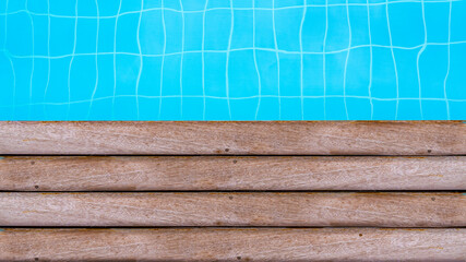 A wooden swimming pool edge with blue tiles and clear water..Top view.