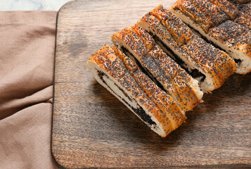 Wooden board with tasty cut poppy seeds bun on light table