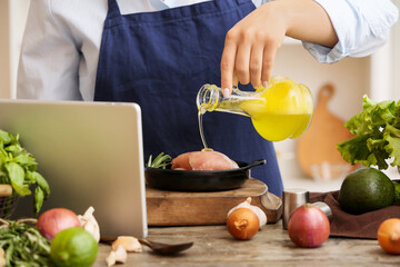 Woman pouring oil onto chicken meat at table in kitchen