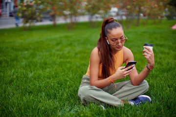 Relaxed young girl using phone apps message online in social network, blogging, create content, sit on lawn outdoors